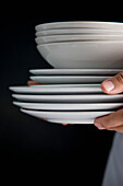 Nahaufnahme von Kellnerhänden, die einen Stapel von Tellern und Schüsseln tragen