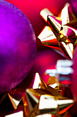 Rote und violette Weihnachtskugeln und goldene Schleifen in extremer Nahaufnahme