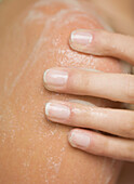 Extreme close up of a woman hand rubbing shower gel on her shoulder