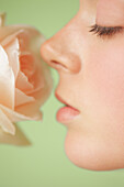 Extreme Nahaufnahme einer jungen Frau im Profil, die eine rosa Rose inhaliert