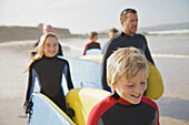 Junge und Mädchen mit Surfbrettern an einem Strand, gefolgt von Menschen