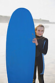Smiling girl holding a surfboard upright