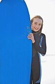 Smiling girl holding a surfboard upright