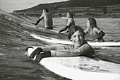 Lächelnder Jugendlicher im Meer, der sich an seinem Surfbrett festhält