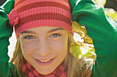 Lächelndes junges Mädchen mit einer Wollmütze und den Händen auf dem Kopf