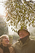 Älteres Paar steht unter einem Baum, schaut nach oben und lächelt