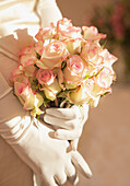 Nahaufnahme einer Braut, die mit behandschuhten Händen einen Rosenstrauß hält