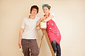 Smiling young couple leaning on a ladder holding paintbrushes