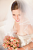 Lächelnde Braut mit Schleier und Rosenstrauß in der Hand