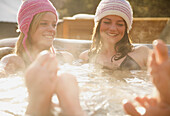 Zwei lächelnde junge Frauen entspannen sich in einem Whirlpool beim Apres-Ski