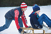 Profile of a  boy pushing a friend sitting on a sled