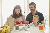 Paar sitzt mit Babyzwillingen am Tisch und benutzt ein digitales Tablet