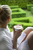 Frau trinkt Cappuccino und schaut in den Garten hinaus
