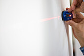 Männerhände halten Laserniveau vor weißer Wand