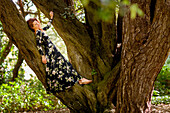 Frau in geblümtem Kleid an Baumstamm gelehnt im Wald