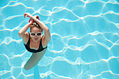 Elevated view of a woman standing in a swimming pool with arms crossed over head