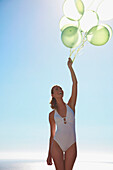 Frau hält ein Bündel grüner Luftballons und lächelt