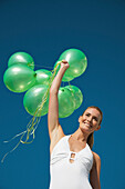 Woman holding a bundle of green balloons smiling - low angle view