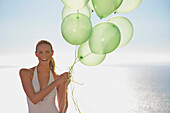 Nahaufnahme einer Frau, die ein Bündel grüner Luftballons hält und lächelt