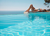 Woman sunbathing by a swimming pool with ocean in the background