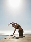 Young woman practicing yoga by a swimming pool with ocean in the background