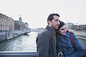 Junges Paar umarmt sich auf einer Brücke über die Seine, Paris, Frankreich