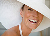 Nahaufnahme einer jungen Frau mit weißem Hut, die lächelt