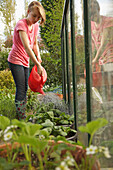 Jugendliches Mädchen gießt Pflanzen in einem Garten