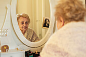 Lächelnde ältere Frau betrachtet ihr Spiegelbild neben einem alten Foto