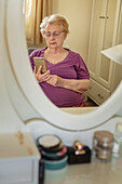 Spiegelbild einer älteren Frau, die zu Hause ein Smartphone benutzt