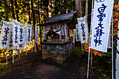 Kleiner Shinto-Schrein in einem Wald, umgeben von weißen Kanji-Bannern, Japan, Asien