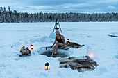 Frau beim Eisbaden auf einem zugefrorenen See in der Abenddämmerung, Jokkmokk, Norrbotten, Schwedisch-Lappland, Schweden, Skandinavien, Europa