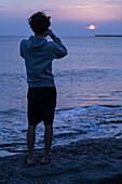 Junge Person am Strand mit Blick auf den Horizont bei Sonnenuntergang in der Normandie