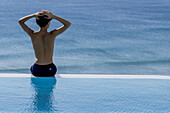Young man sitting on edge of swimming pool near the sea