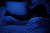 Schwach beleuchtete Aufnahme einer Person, die sich im Schlaf an ein Kissen schmiegt