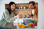 Erwachsenes Paar, das sich beim Frühstück über sein Smartphone unterhält