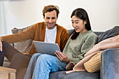 Adult couple using digital tablet while sitting on sofa