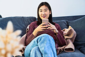 Junge erwachsene Frau schaut in die Kamera, während sie ein Smartphone benutzt