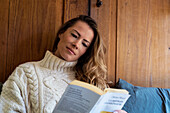 Junge erwachsene Frau, die auf dem Bett liegend ein Buch liest