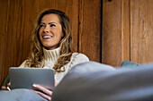Low angle view of adult woman using digital tablet while sitting on bed