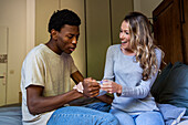 Surprised man looking at pregnancy test while sitting next to girlfriend