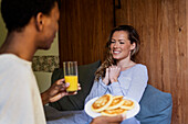 Glückliche Frau auf dem Bett liegend, während ihre Freunde sie mit einem Frühstück überraschen