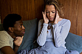 Erwachsene Frau mit Kopfschmerzen, während sie sich mit ihrem Freund im Bett unterhält