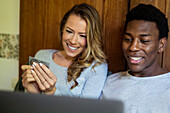 Glückliches Paar beim Online-Shopping auf dem Laptop im Bett liegend