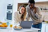 Erwachsenes Paar benutzt Laptop, während es in der Küche steht
