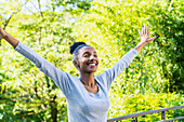 Young adult woman raising arms while smiling standing outdoors