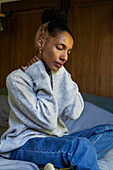 Gestresste junge erwachsene Frau, die ihren Nacken berührt, während sie im Bett sitzt