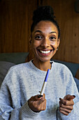 Junge erwachsene Frau lächelt in die Kamera, während sie einen Schwangerschaftstest hält