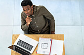 Zenitansicht eines nachdenklichen Geschäftsmannes, der am Schreibtisch sitzt und an einem Laptop arbeitet