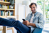 Businessman using smart phone while sitting on chair with feet on table